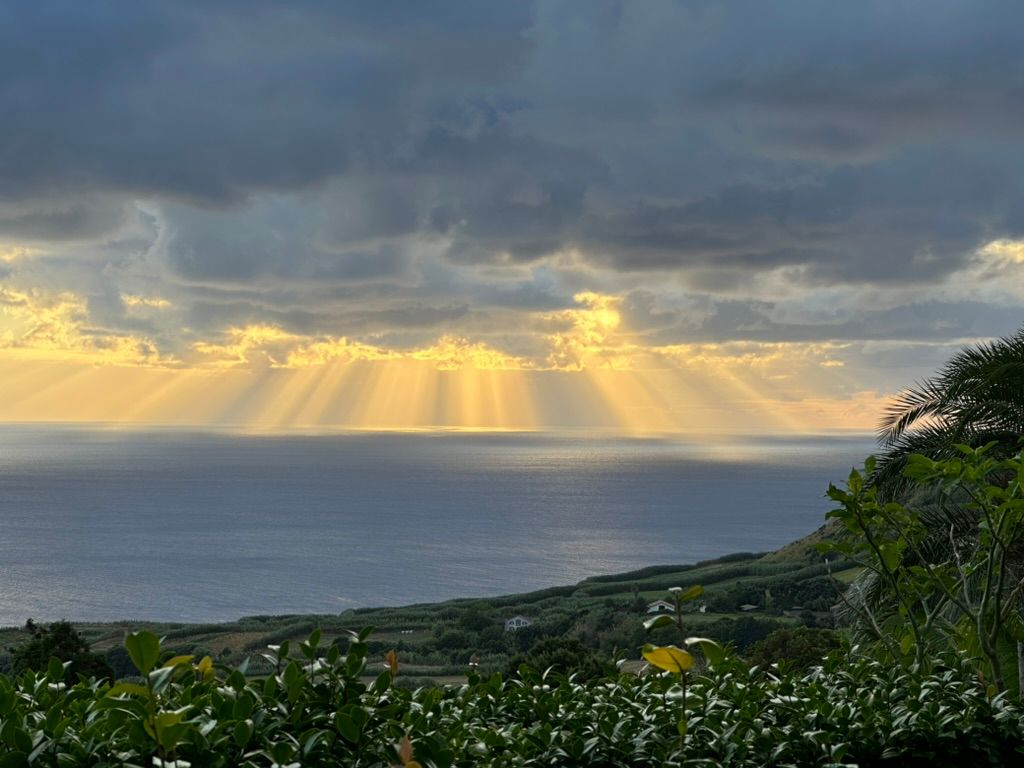 Sunlight breaking through clouds over the ocean and a green hillside.